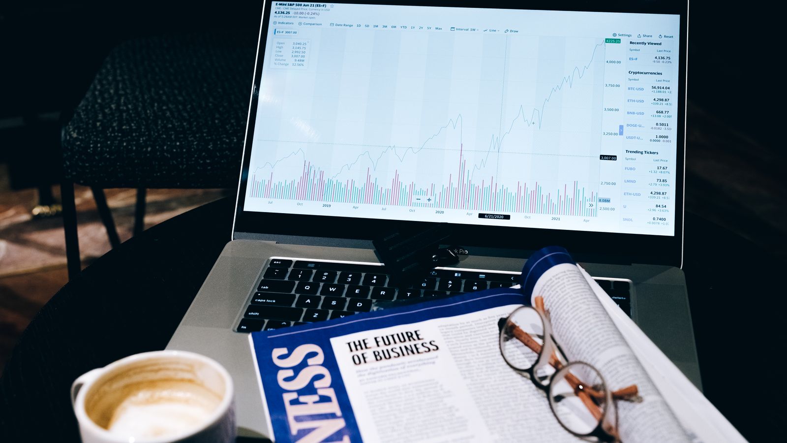 Un espace de travail moderne avec un ordinateur portable affichant des données boursières, à côté d'un magazine professionnel et d'un café.