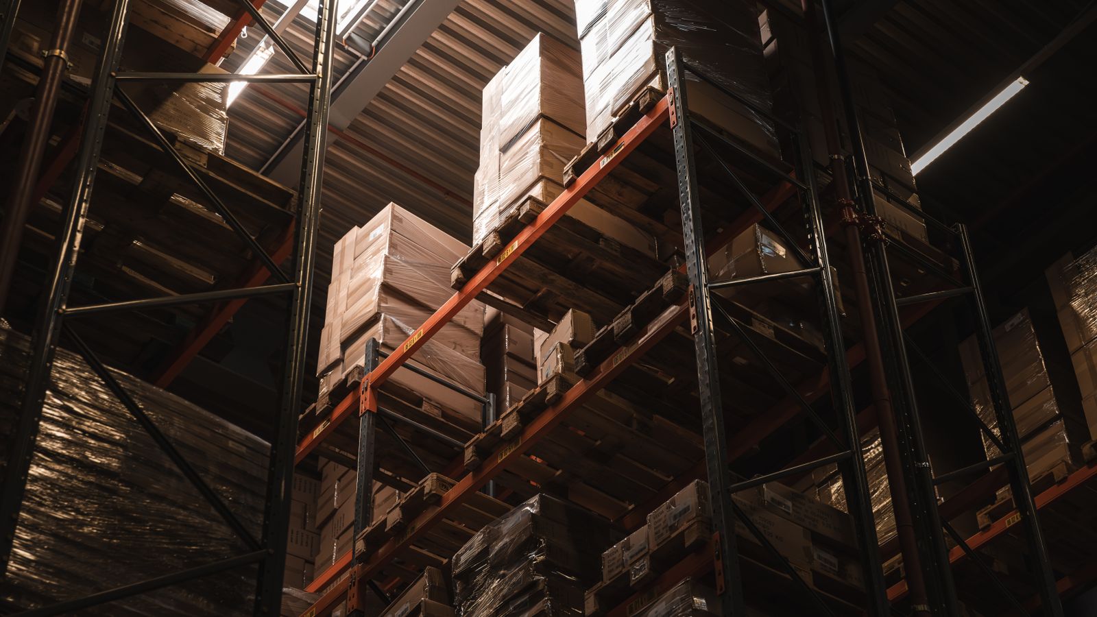 Vue intérieure d'un entrepôt avec des cartons empilés sur des étagères hautes, illustrant le stockage et la logistique.