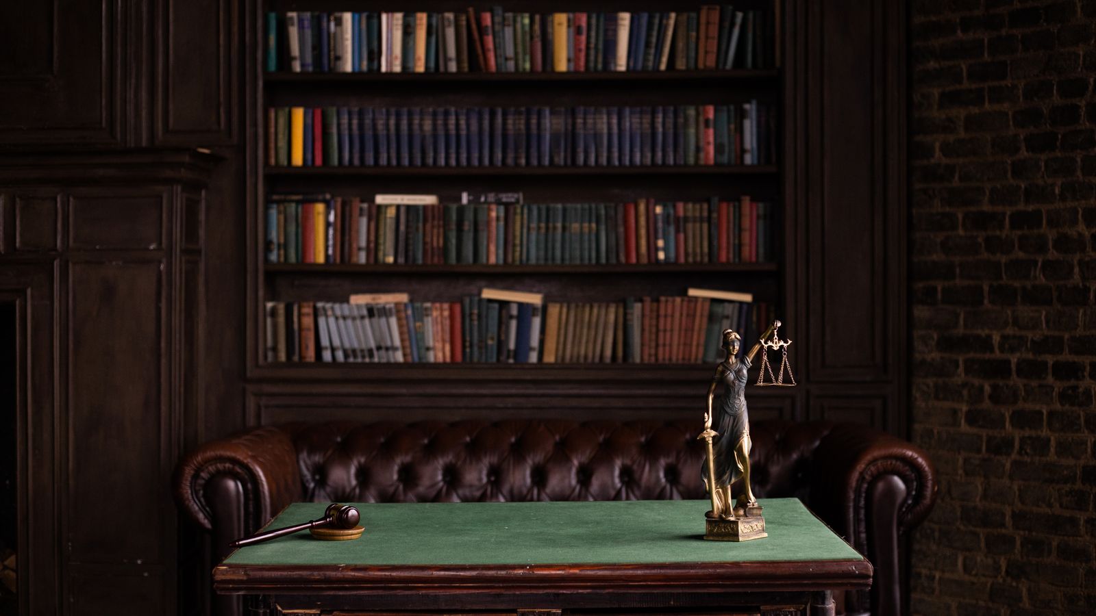 Une salle d'étude classique avec des étagères de livres, un maillet et une figurine de la Justice sur une table verte.