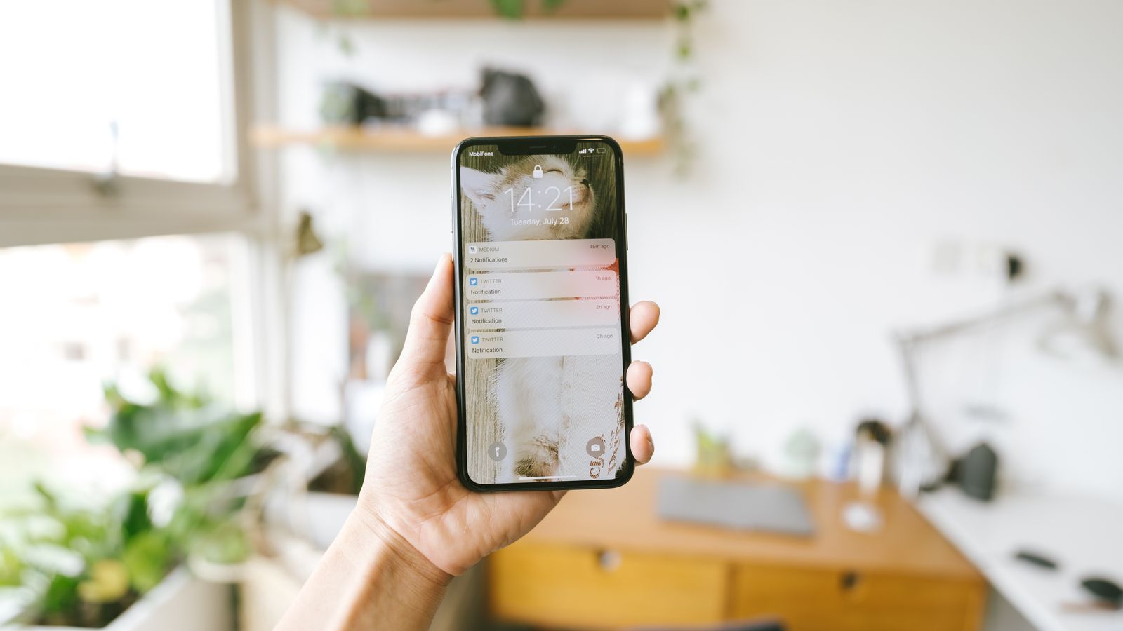 Main tenant un smartphone à l'intérieur avec un arrière-plan de bureau flou, mise au point sur les notifications de l'écran.