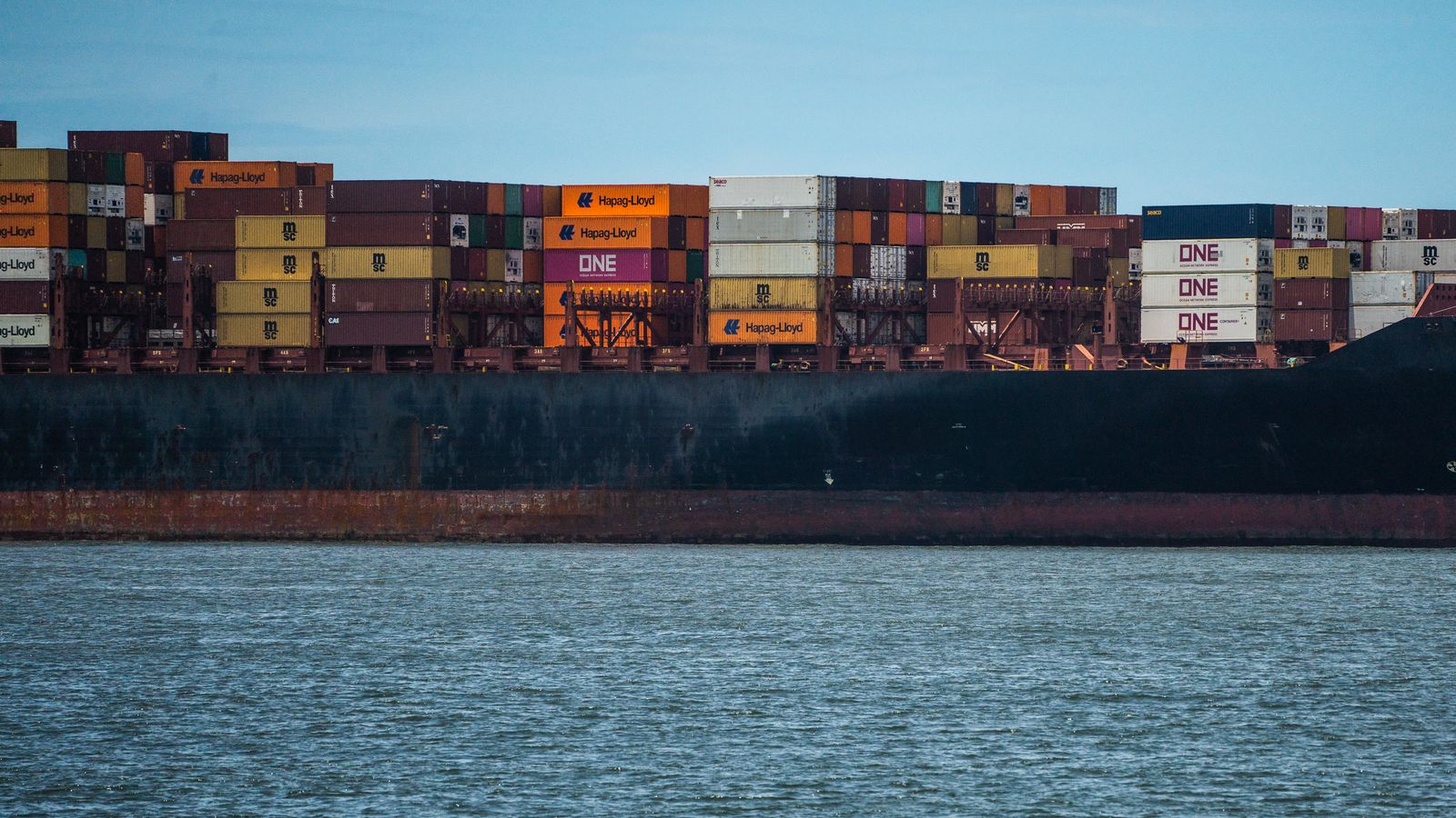 Grand cargo chargé de conteneurs colorés sur une mer calme sous un ciel clair.