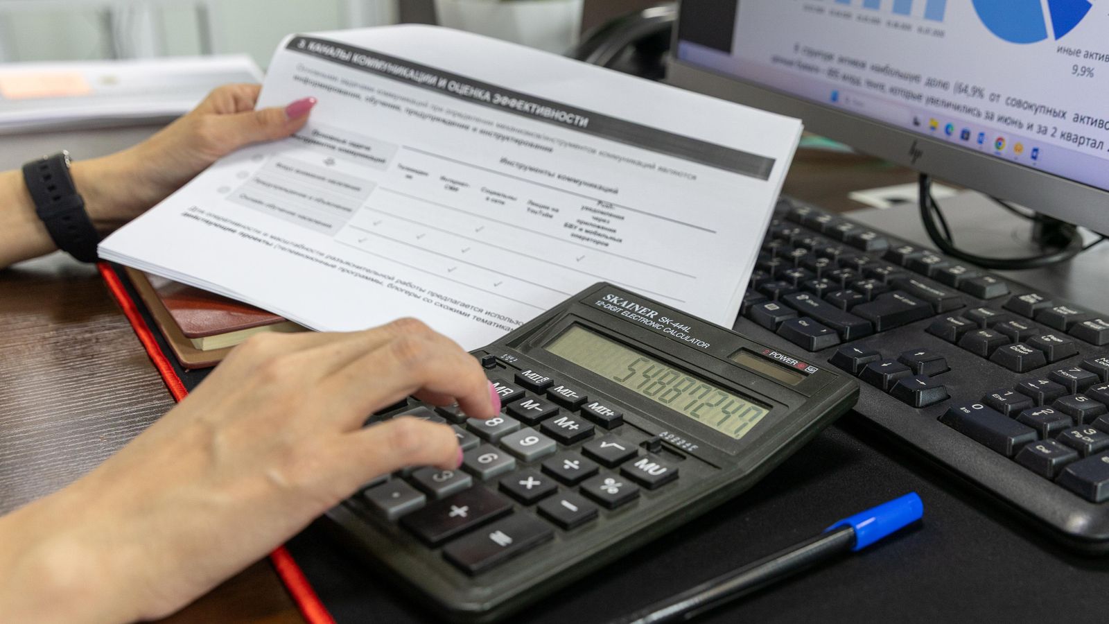 Une personne calcule des données financières à l'aide d'une calculatrice et d'un document, travaillant à un bureau.